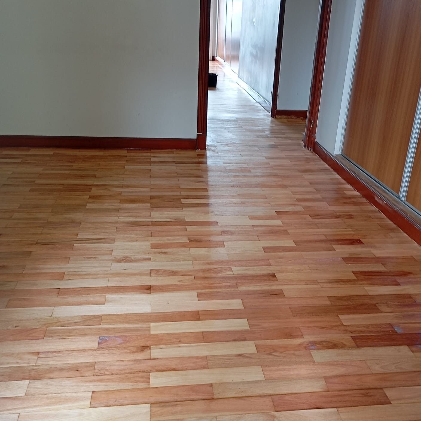 Suelo de madera en una habitación con una pared clara y un armario. Molduras marrones alrededor de las puertas.