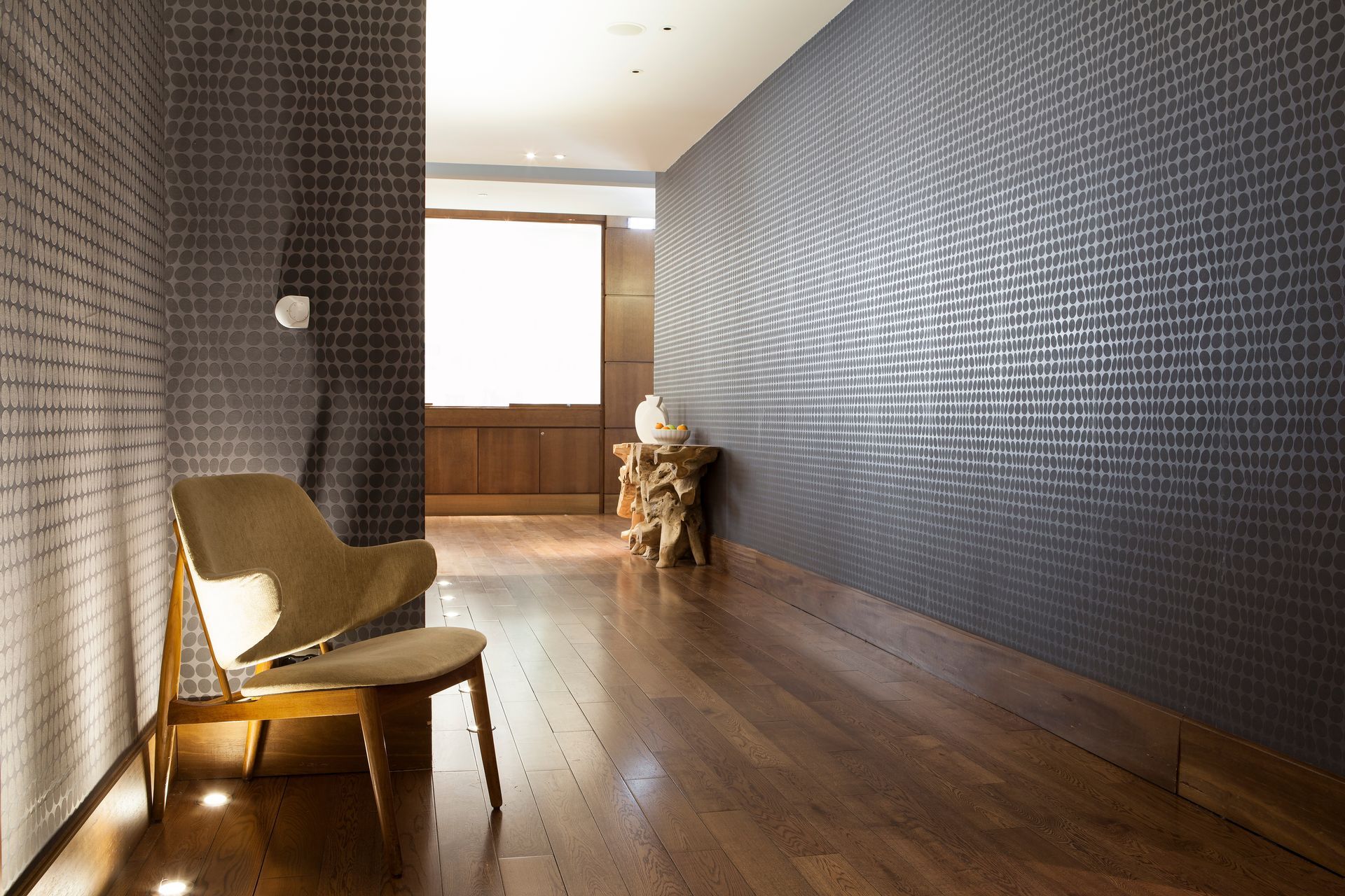 Long hallway with dark textured walls, wooden floor, and a chair by a bright window at the end. Long hallway with dark textured walls, wooden floor, and a chair by a bright window at the end.