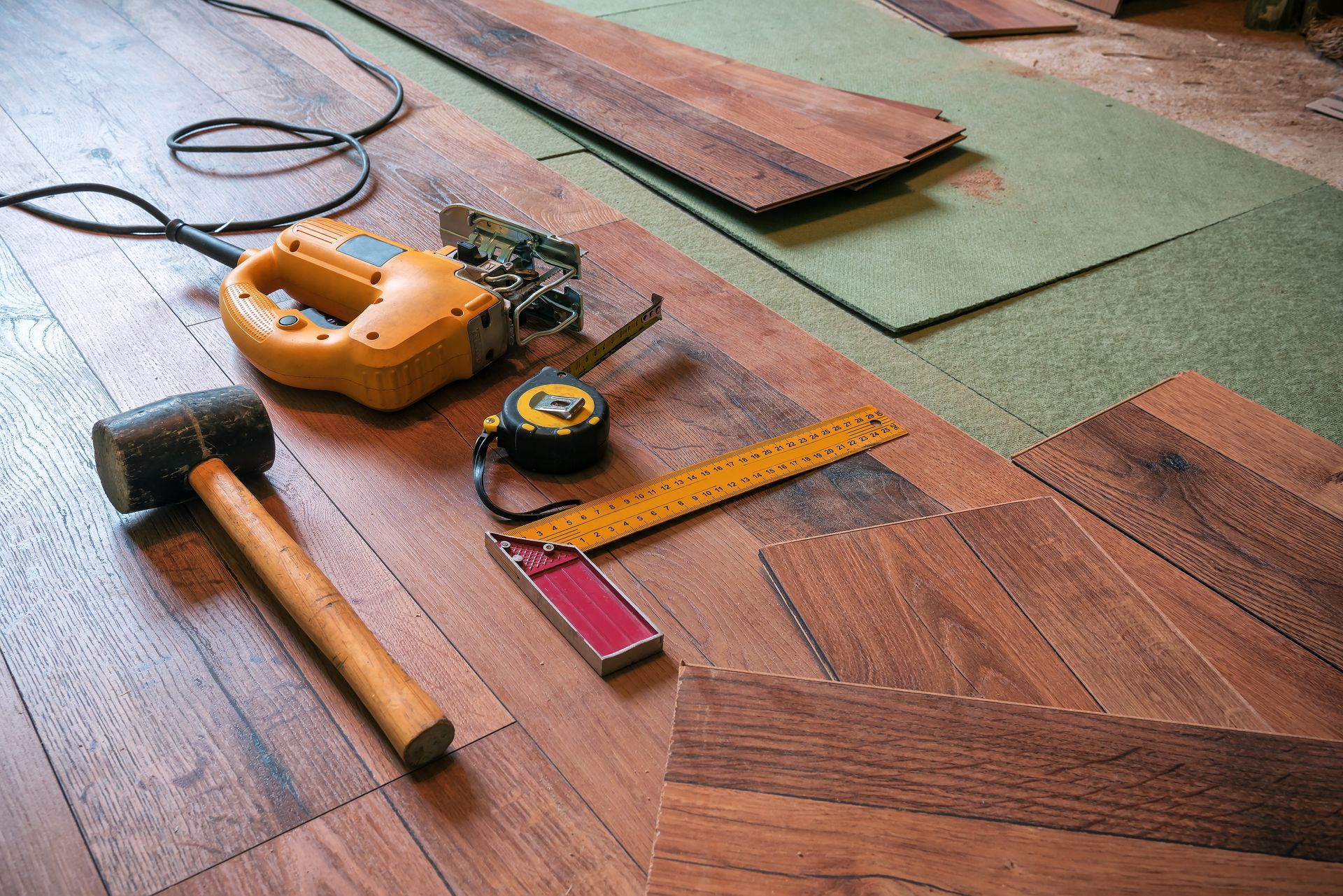 Tools on a wooden floor: hammer, tape measure, saw, ruler, and power tool.