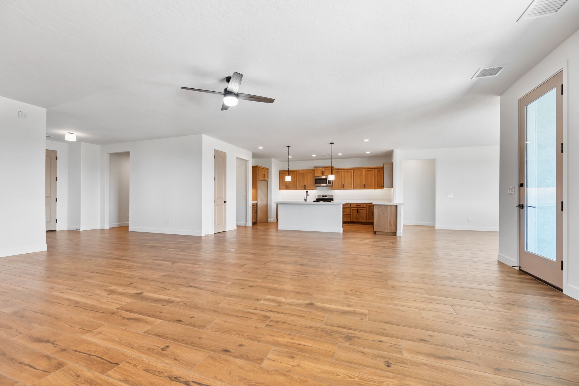 Spacious empty living room with wood floors, white walls, and a kitchen opening in the background.