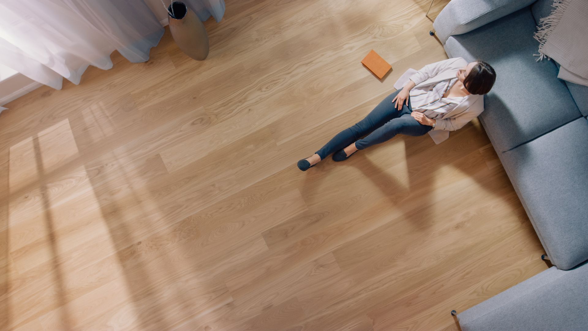 Person reclining on a light blue sofa in a bright room with a wooden floor.