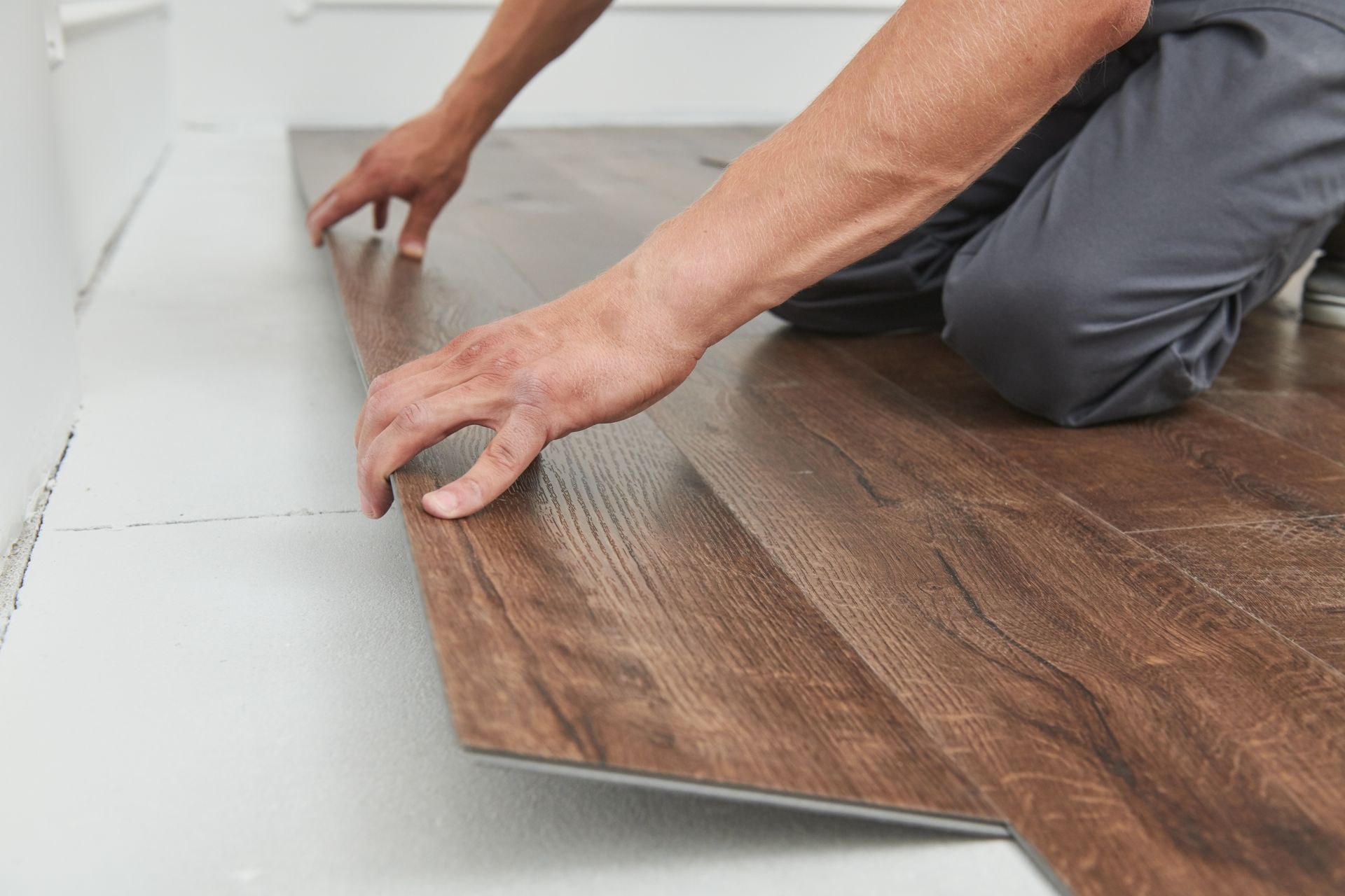 Hands installing a wood-look floor plank over a gray subfloor Hands installing a wood-look floor plank over a gray subfloor