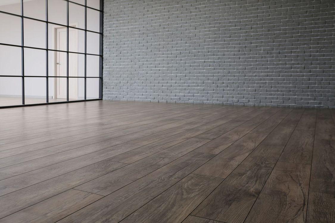 Empty room with wooden floor, gray brick wall, and black-framed windows