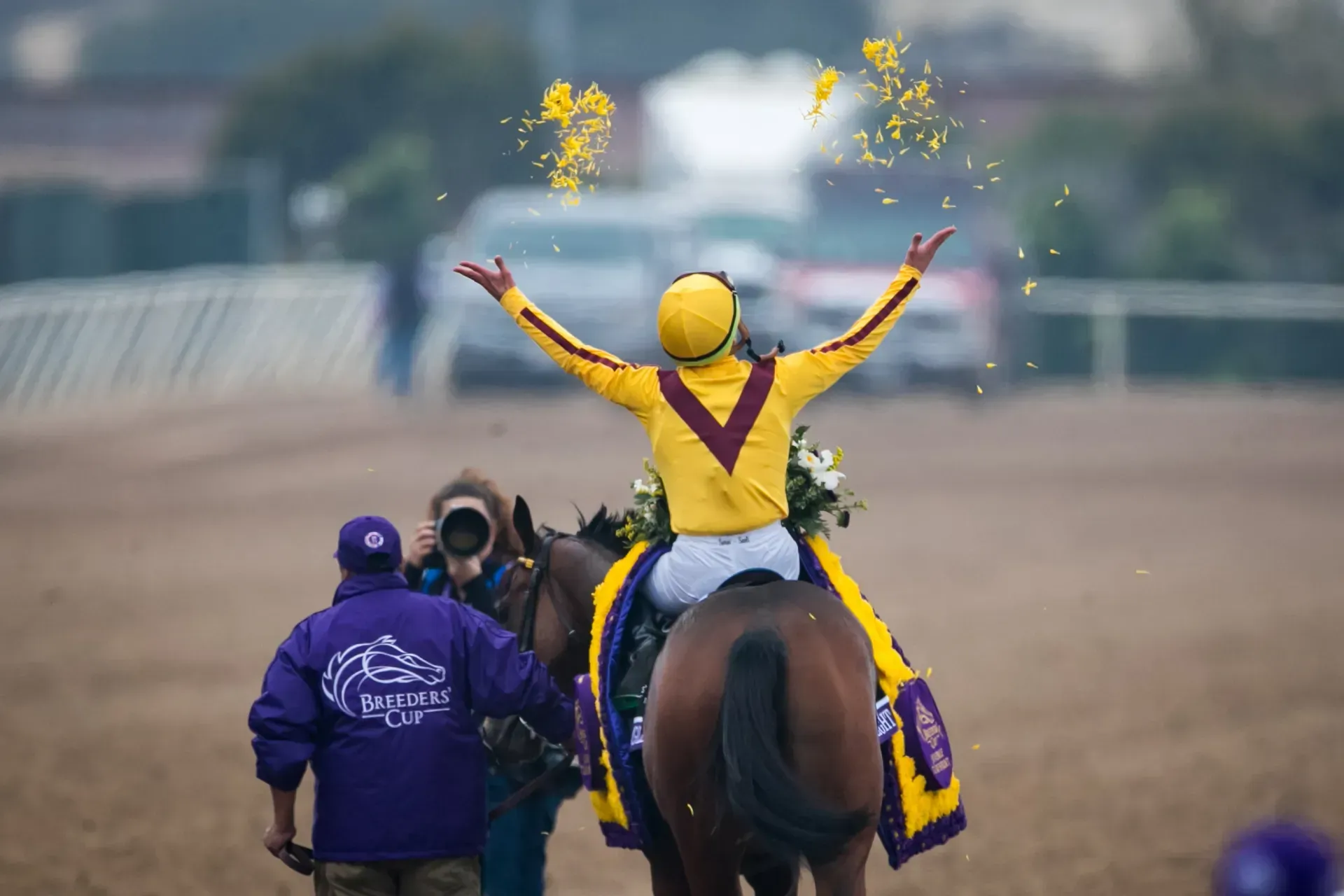 A jockey is riding a horse with his arms in the air.