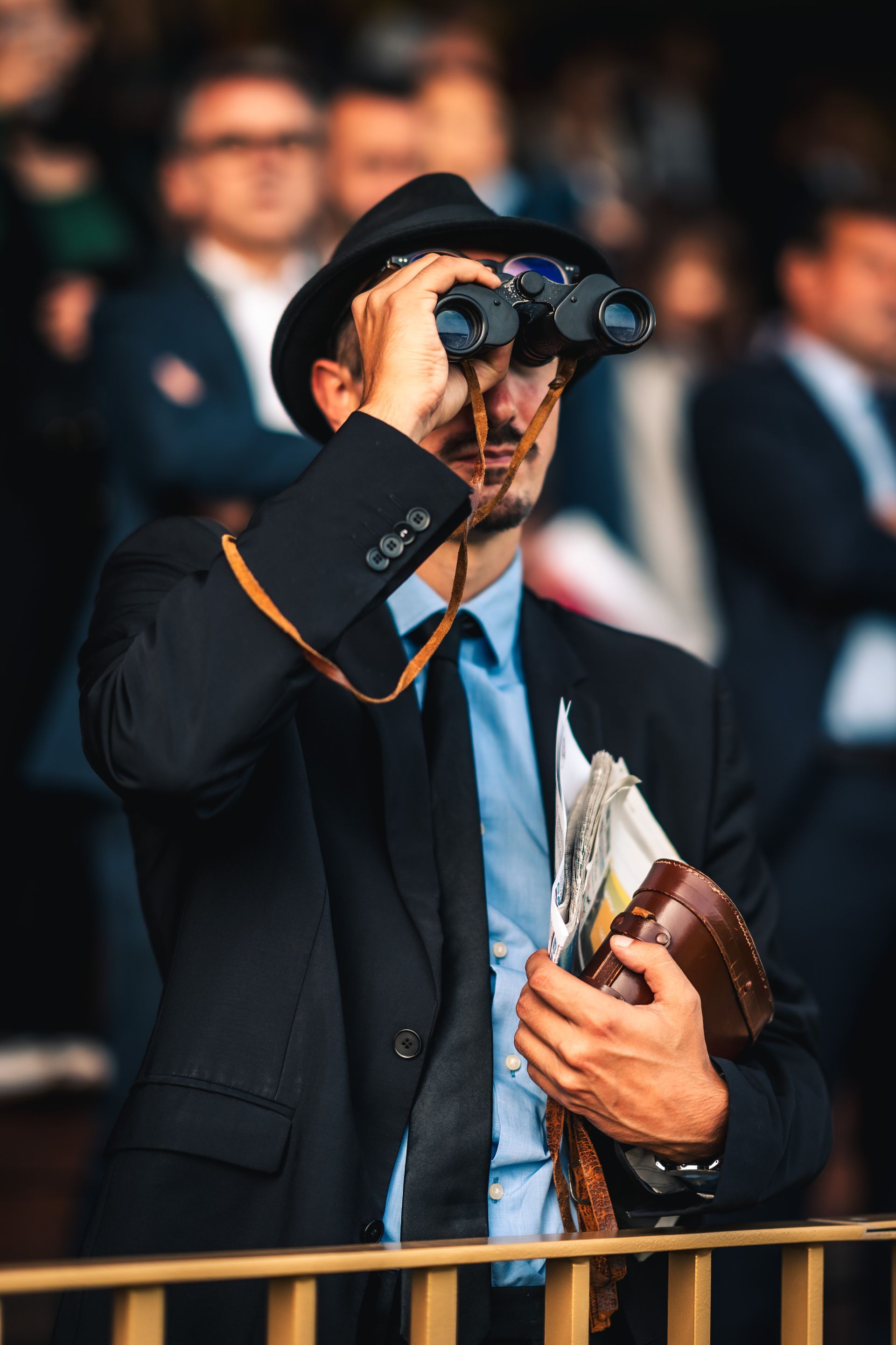 A man in a suit and hat is looking through binoculars.