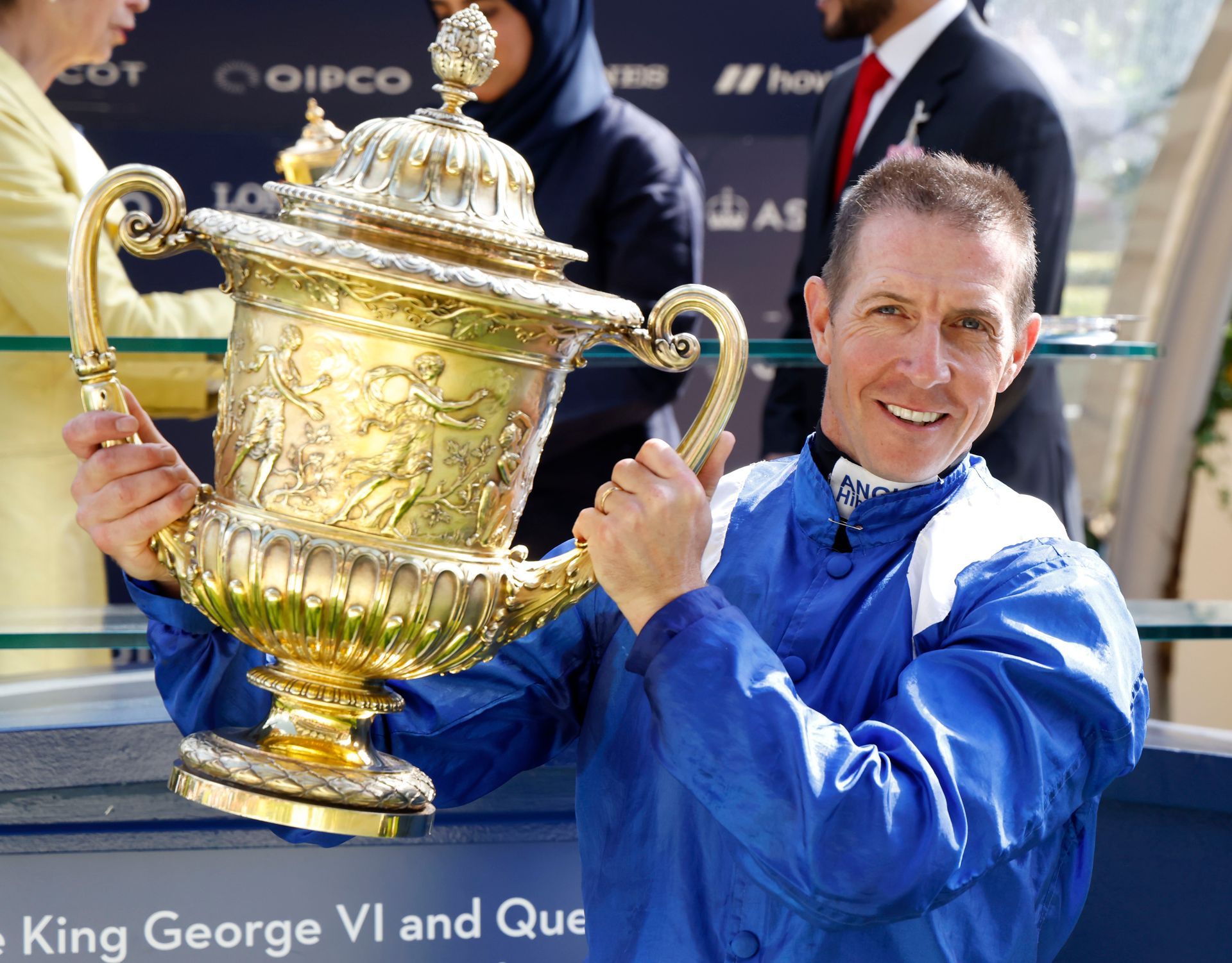 A man in a blue jacket is holding a large trophy
