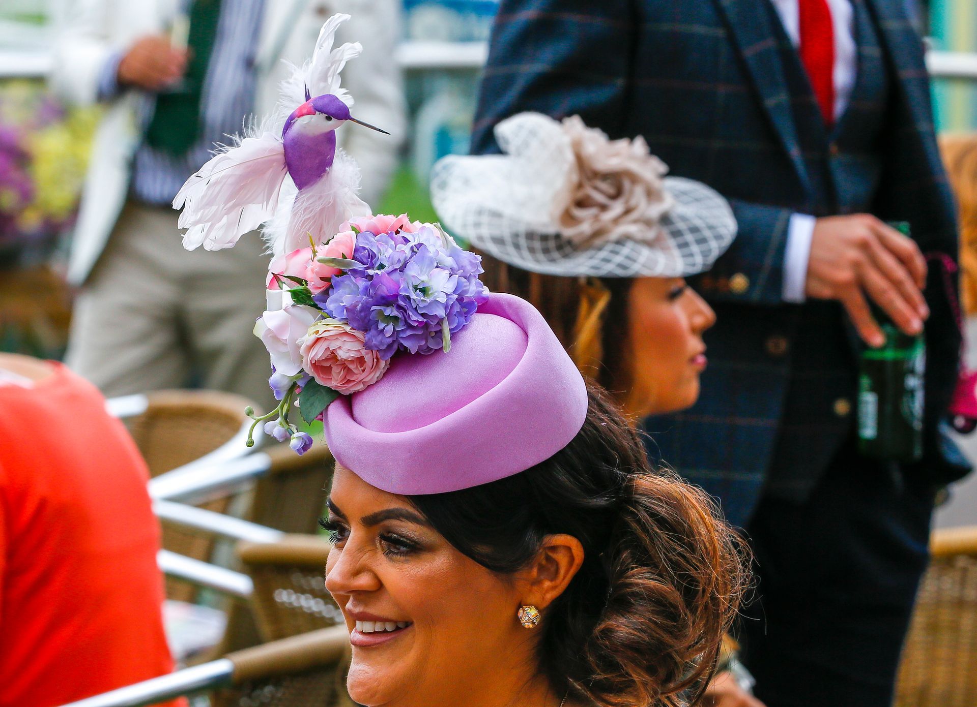 A woman wearing a purple hat with flowers on it is smiling.