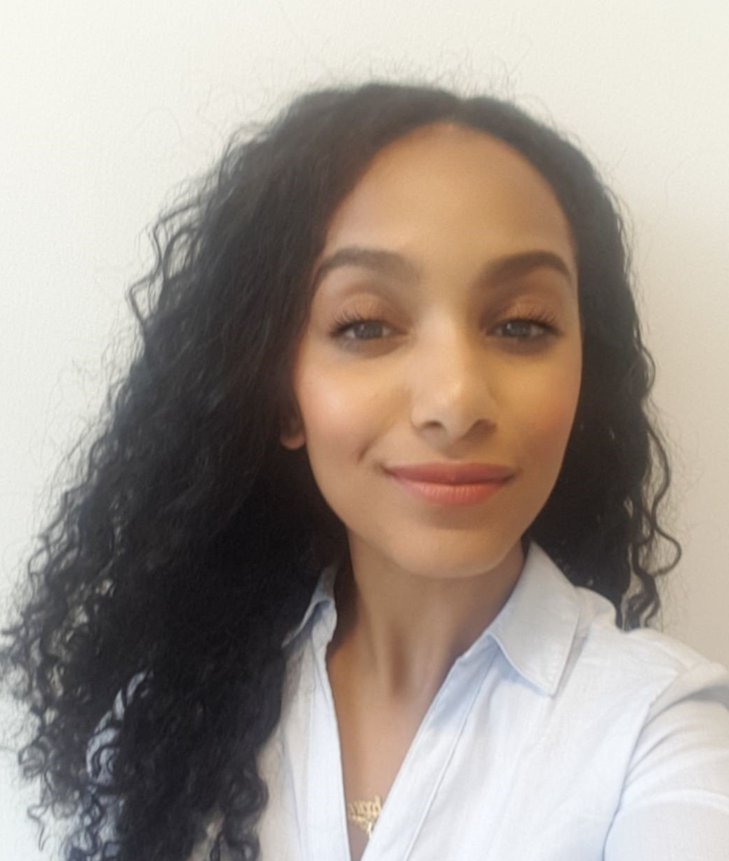 A woman with curly hair is smiling and wearing a white shirt