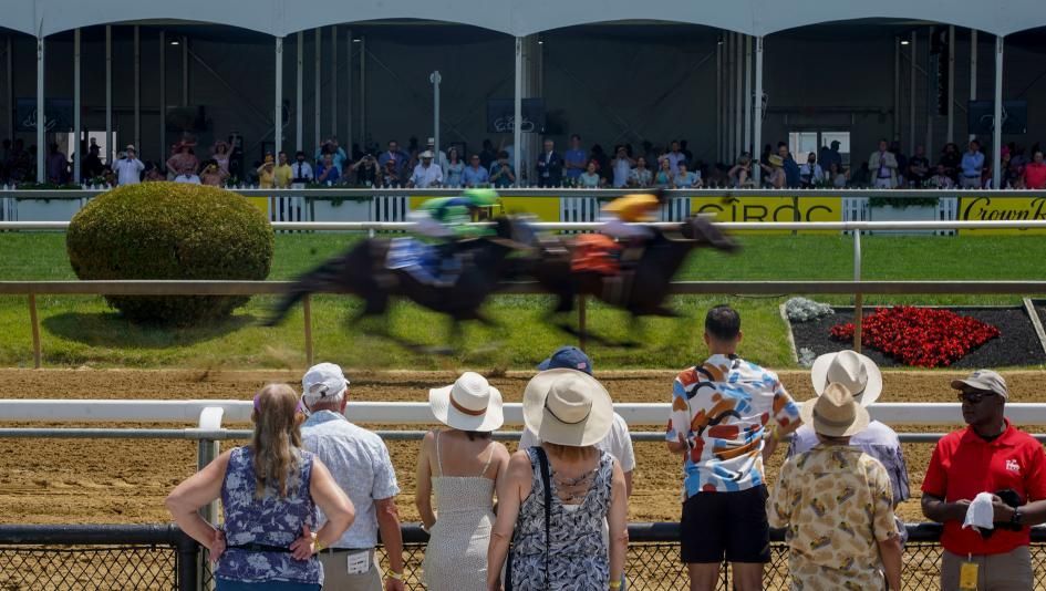 A group of people are watching a horse race on a track.