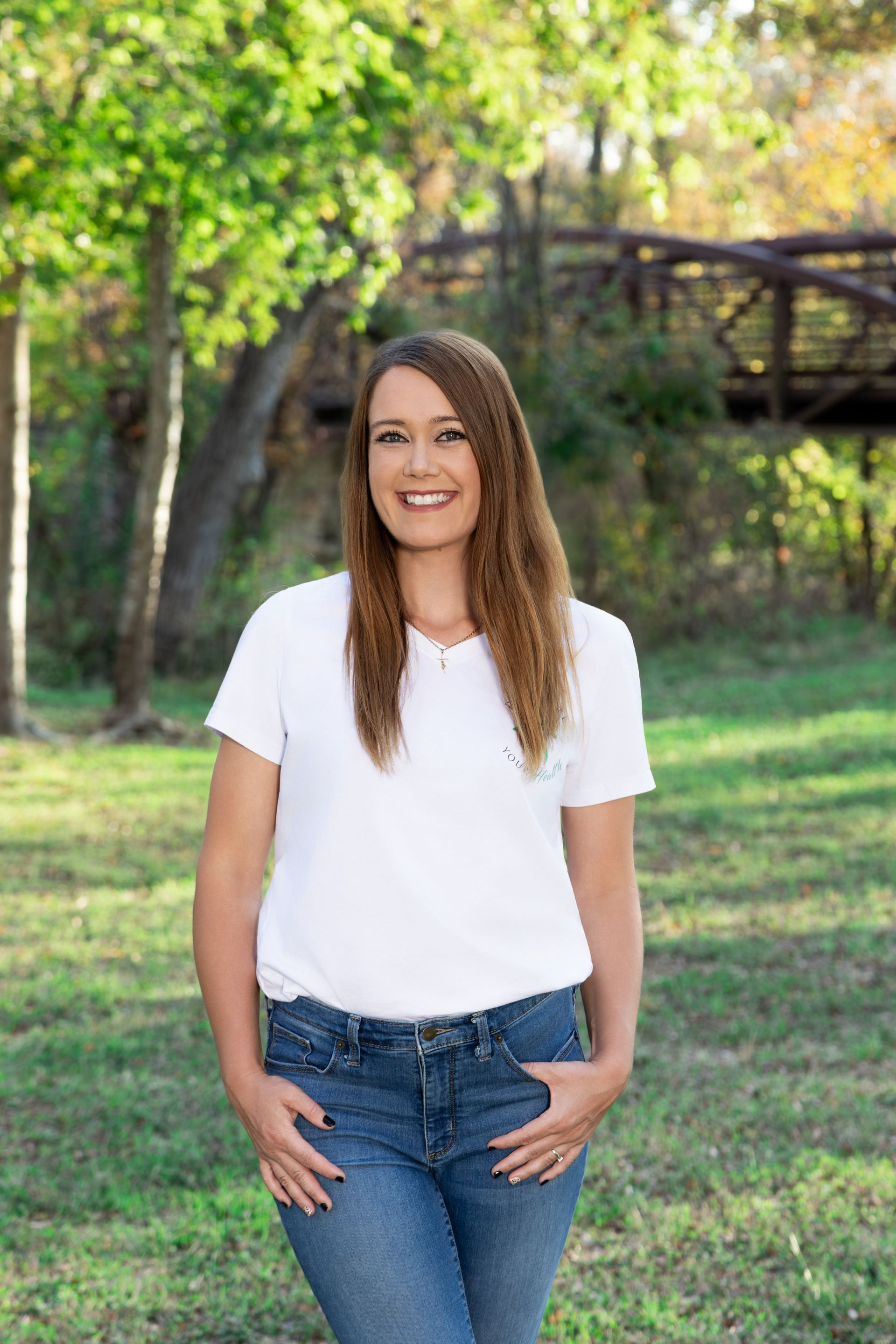 Woman in white shirt and jeans smiling outdoors in autumn.