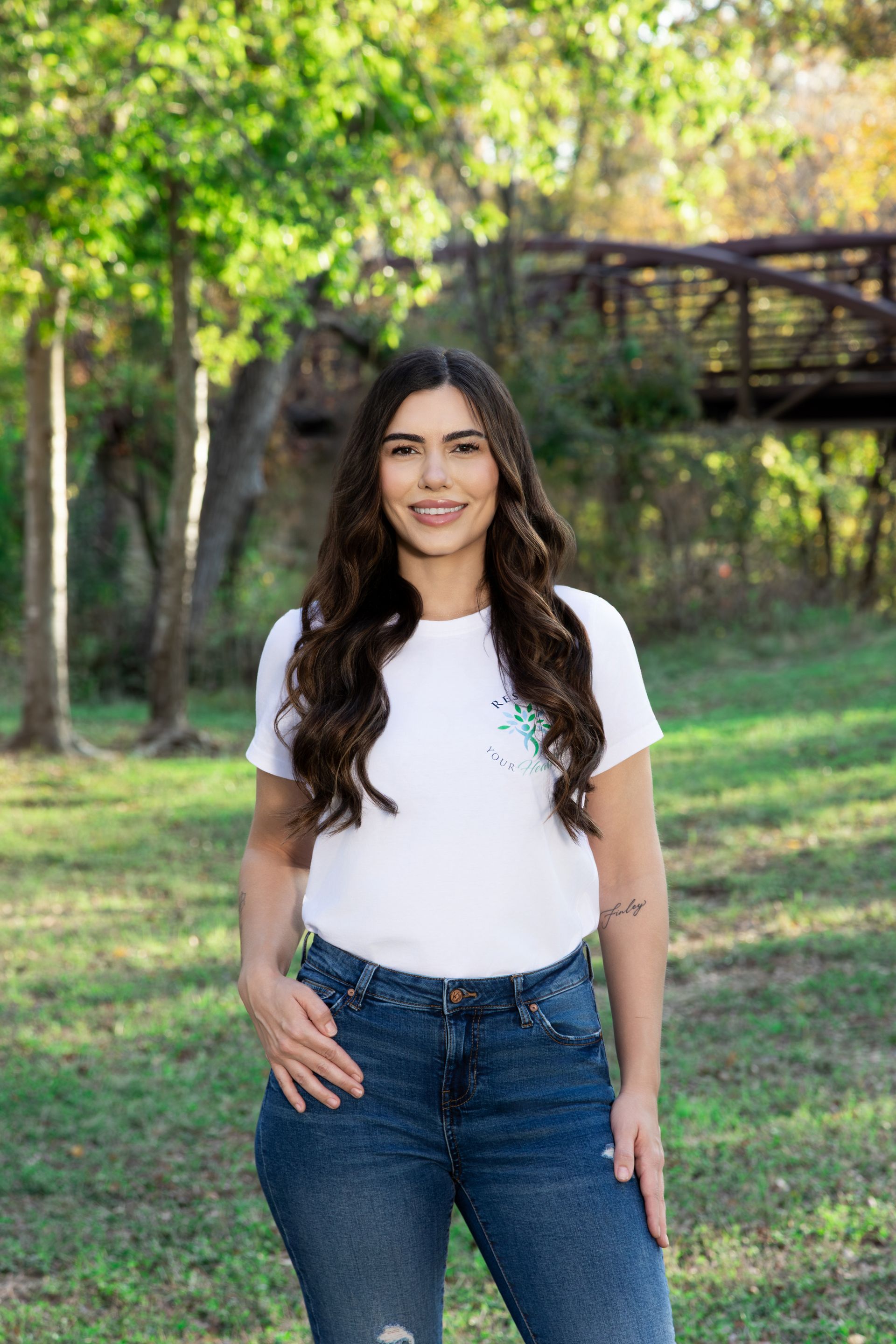 Woman in white shirt and jeans smiling outdoors in autumn.