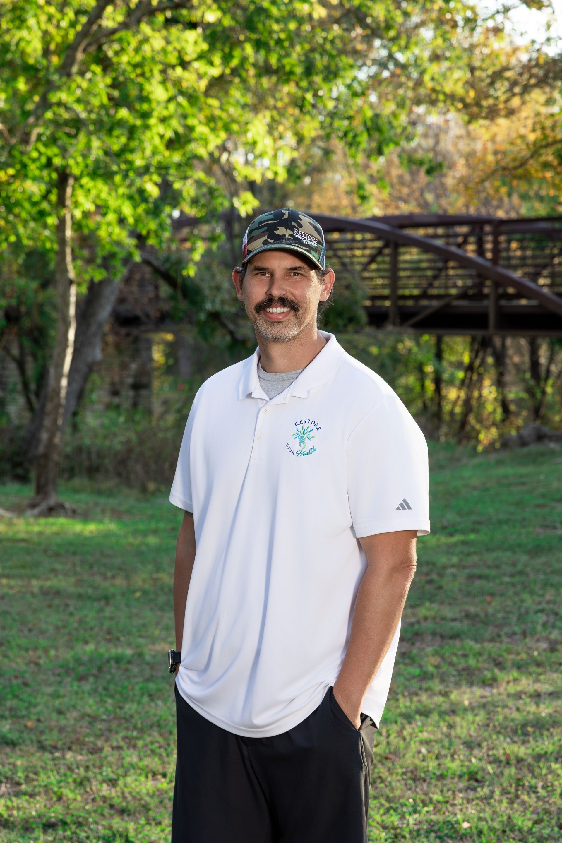 Woman in white shirt and ripped jeans smiling outdoors in a wooded area.