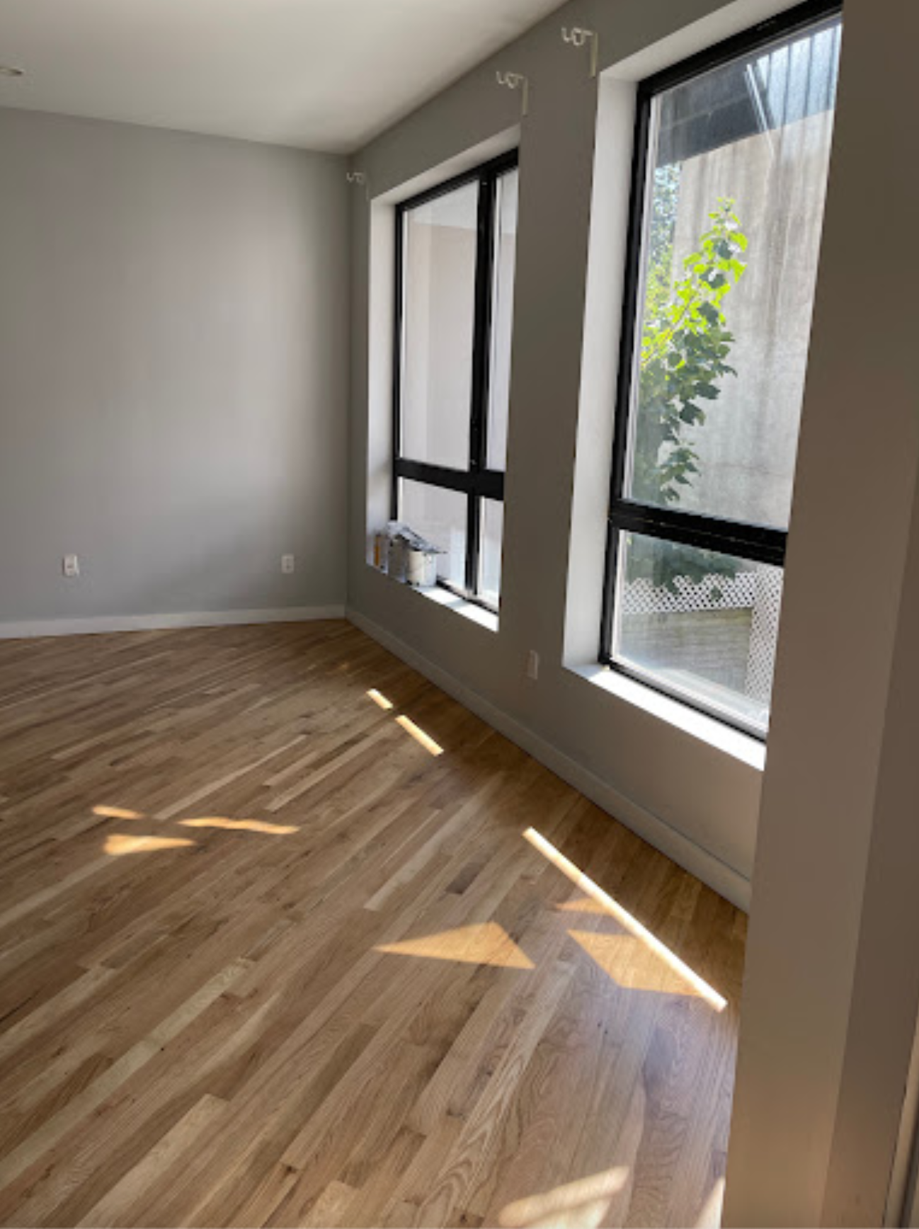An empty room with hardwood floors and two windows.