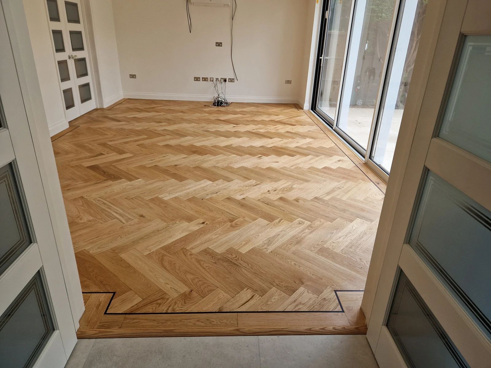 Herringbone wooden floor in a room with glass doors and a decorative border at the doorway.