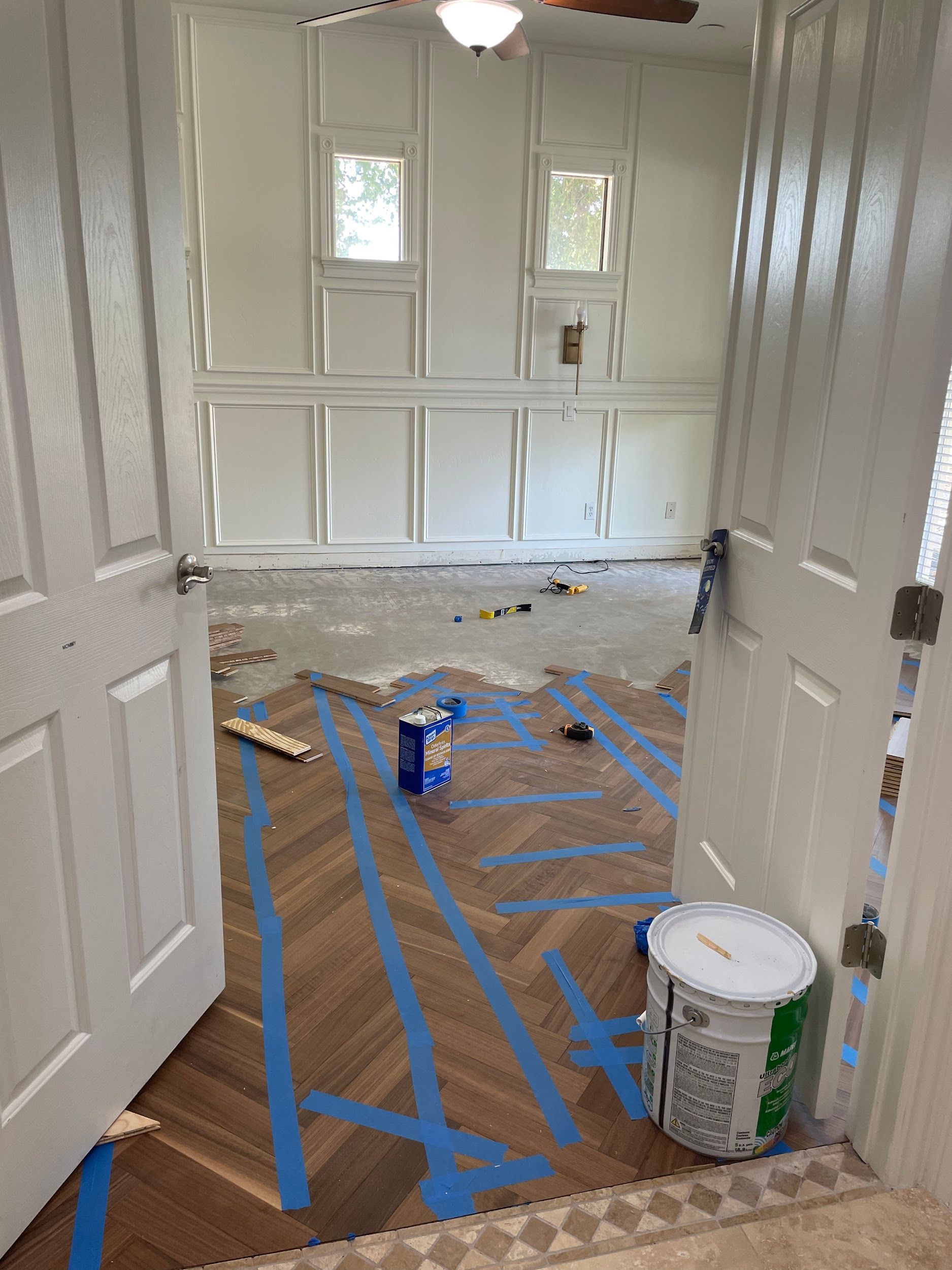 A room with blue tape on the floor and a bucket of paint.