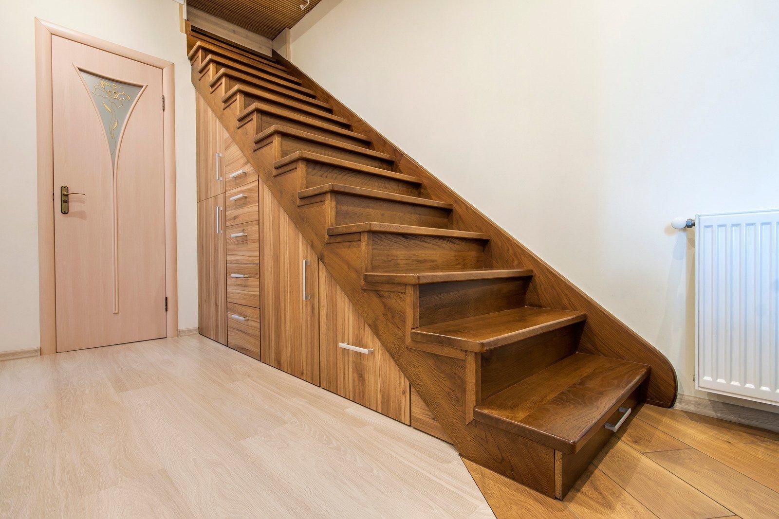 Wooden staircase with storage underneath, leading upwards. Light wood door and flooring.