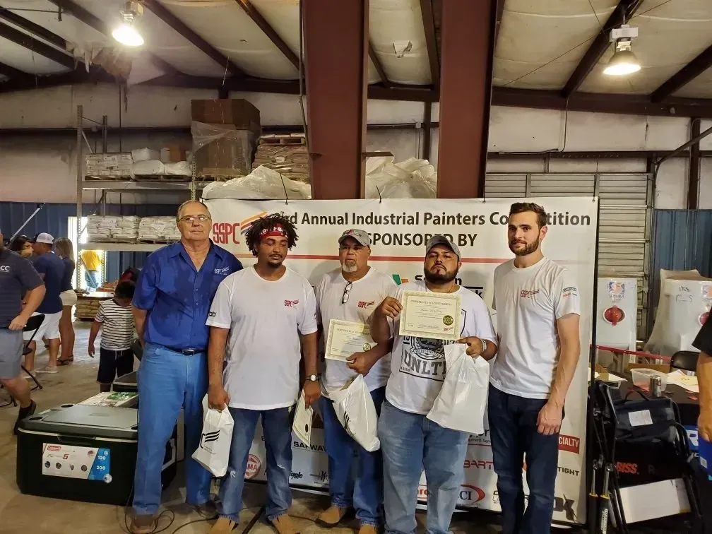 A group of men standing in front of a sign that says industrial painters competition
