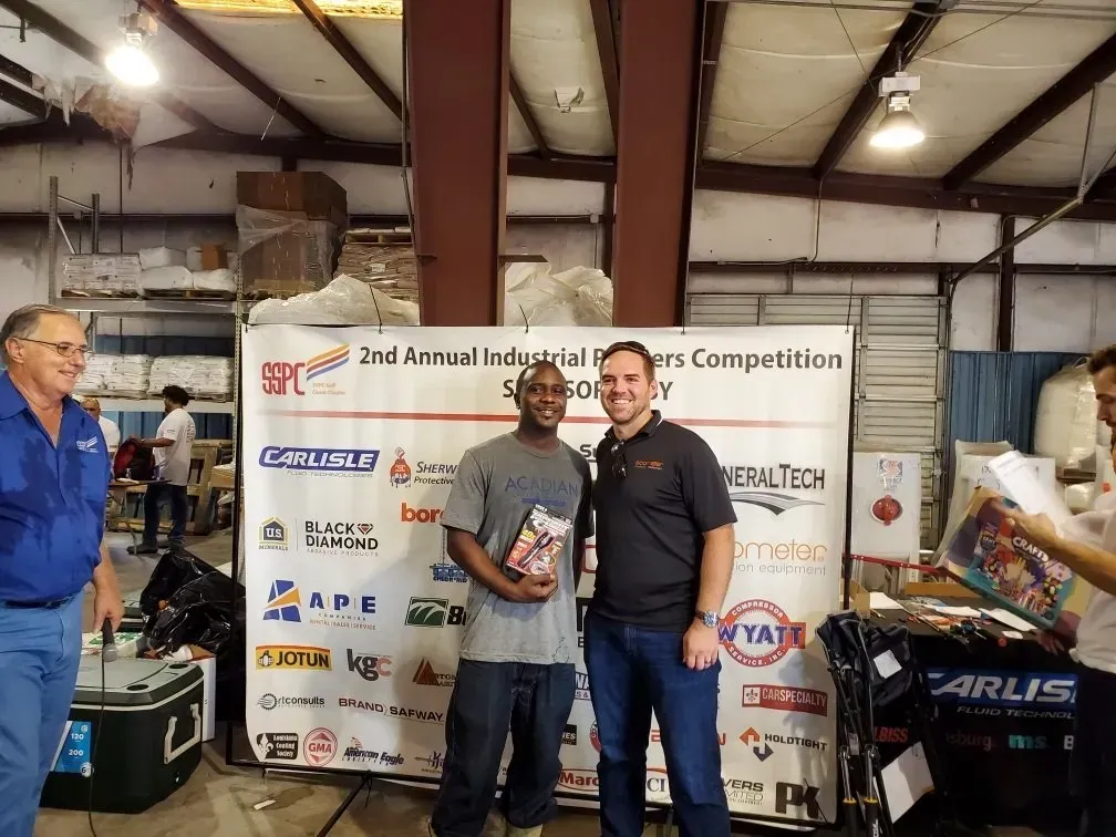 Three men are standing in front of a sign that says 2nd annual industrial workers competition