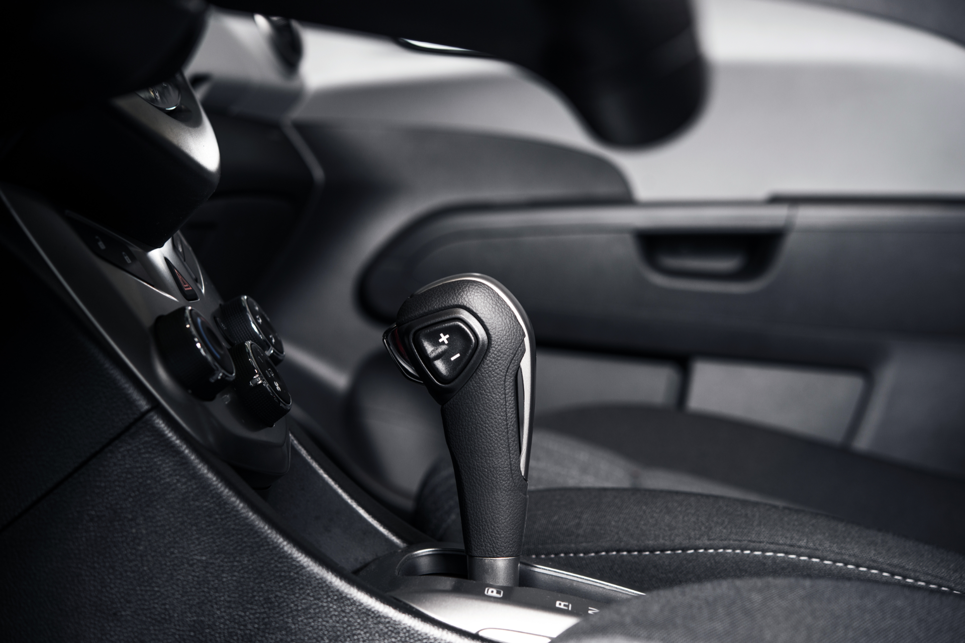 Car's interior with automatic gear shift lever prominent. Black and white photo.