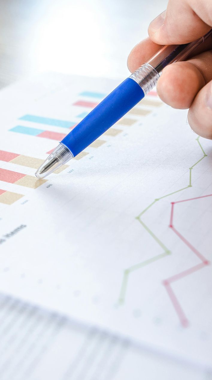 Hand with blue pen pointing at financial bar graphs and line charts.