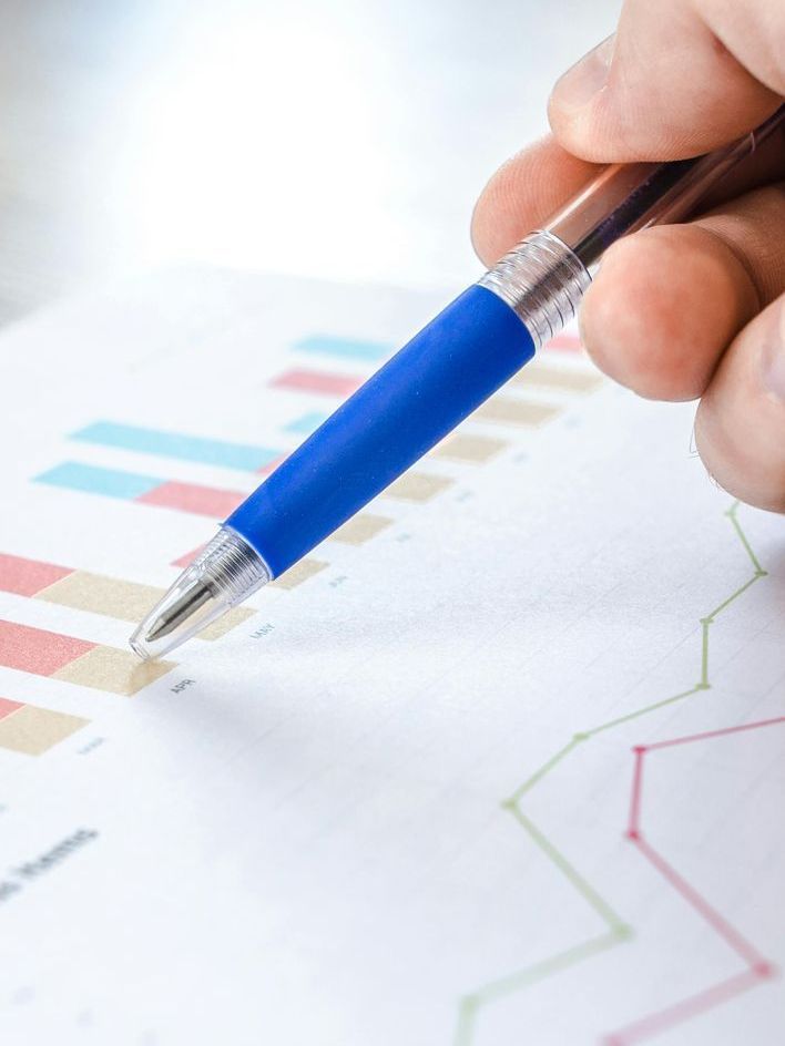 Hand with blue pen pointing at a bar graph and line graph, examining data.