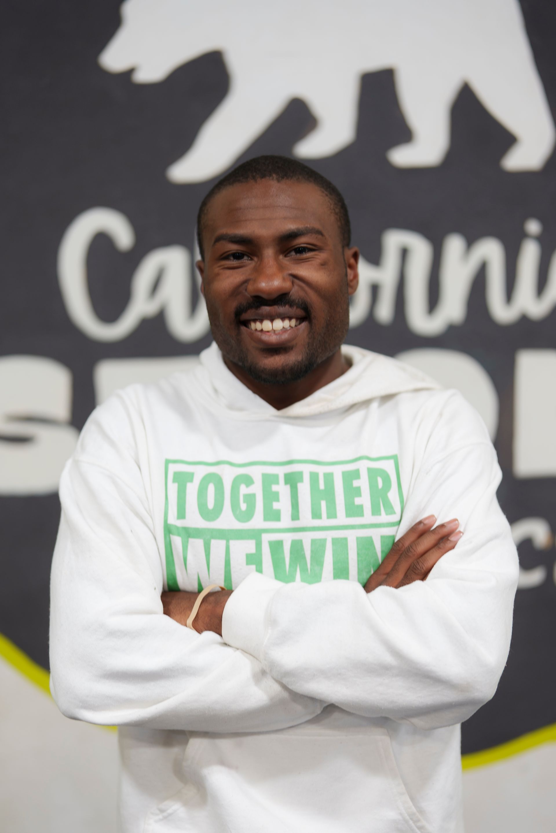 Man in white hoodie with arms crossed smiling in front of a California logo that says 