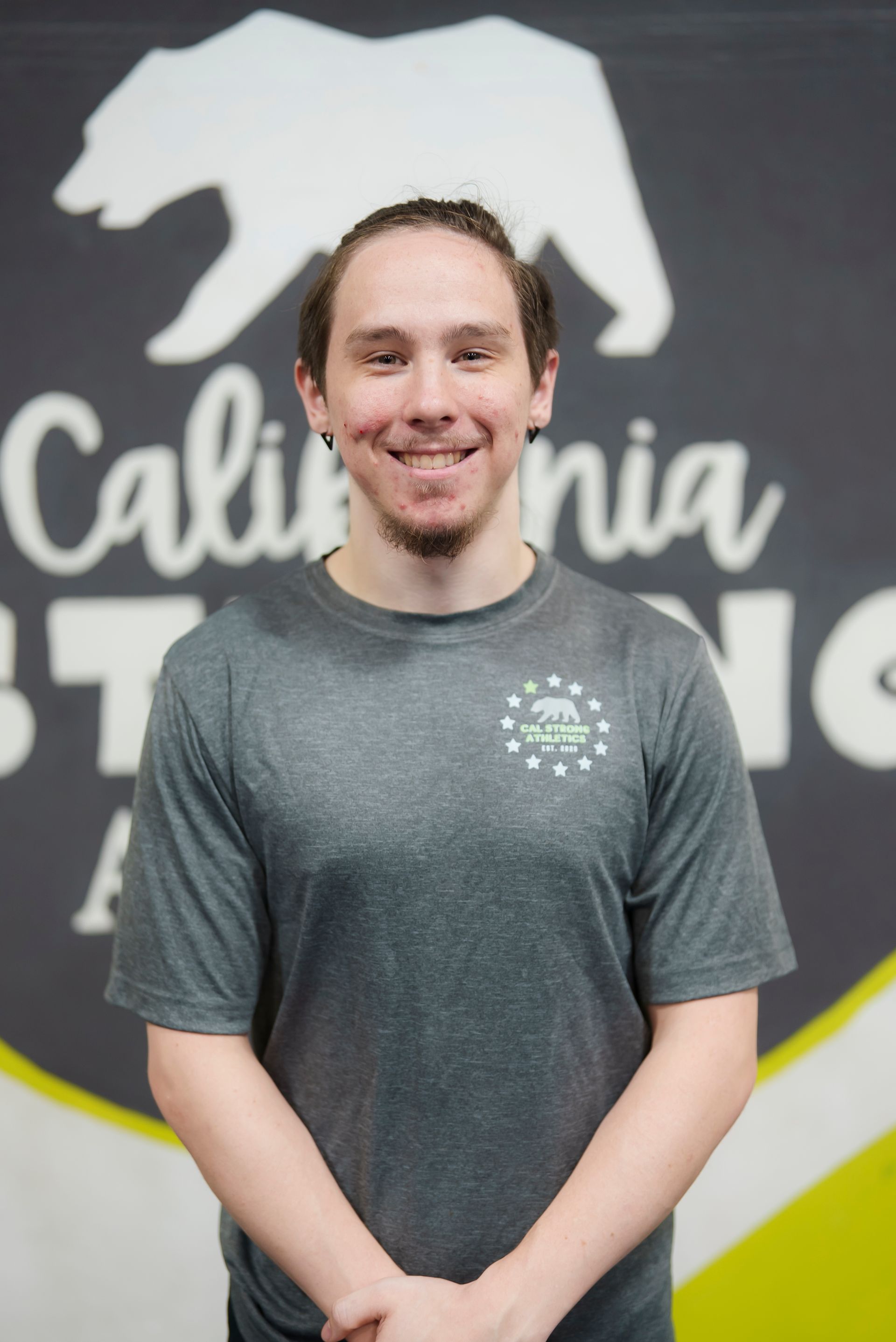 Man with a beard smiles at the camera, wearing a gray shirt with a logo in front of a wall with a bear silhouette.