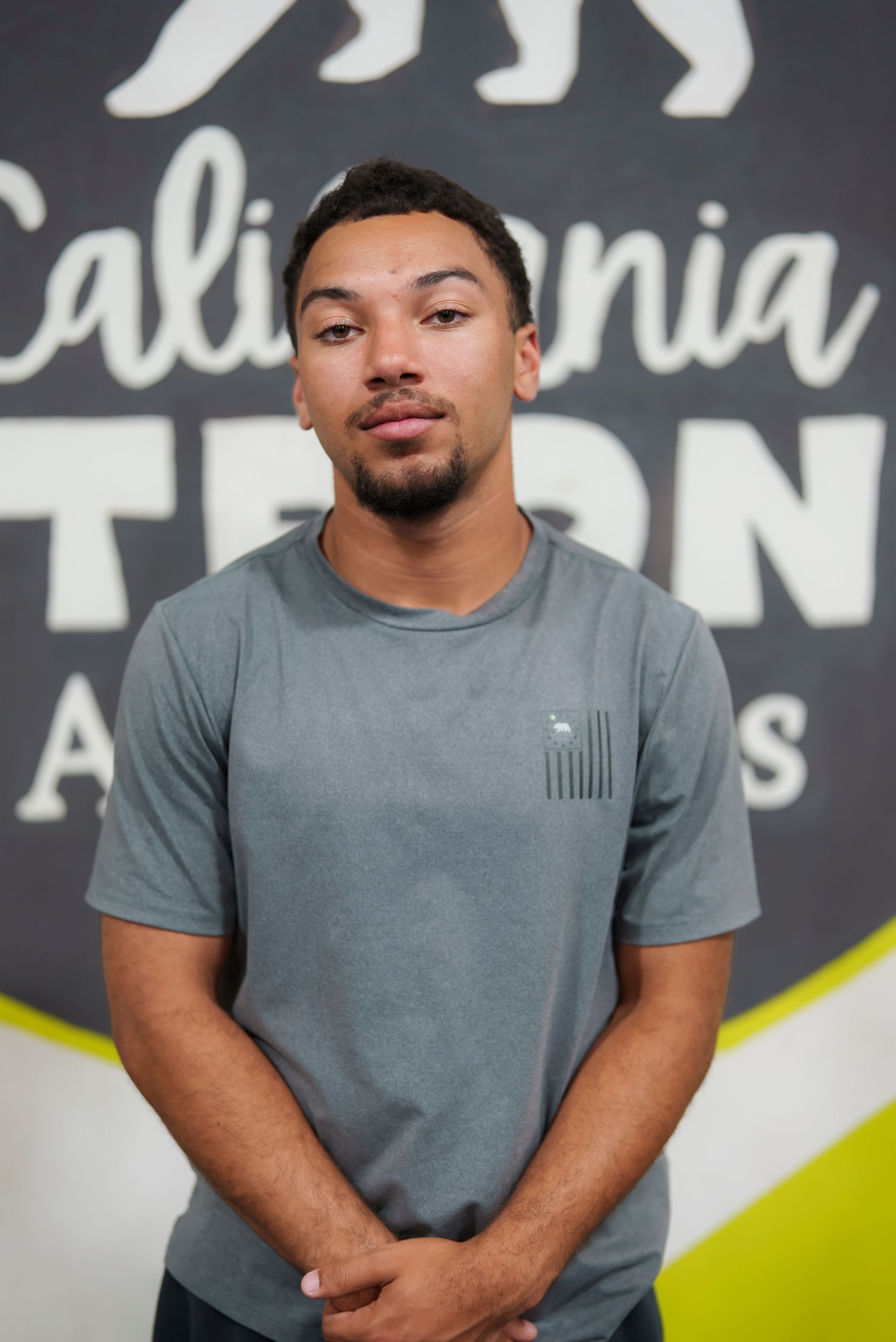 Man with short hair, wearing grey shirt, stands in front of a California Strong Athletics logo.