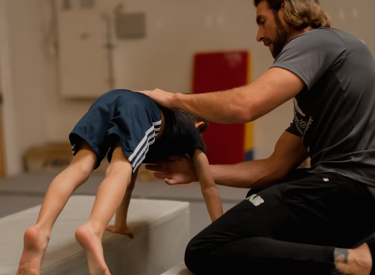A young boy in an orange shirt is climbing a rope