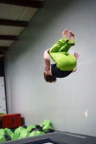 A gymnast in a purple leotard is standing on a balance beam