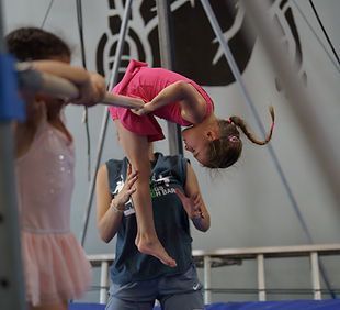 A young girl is sitting on a balance beam in a gym.
