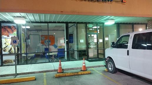 Exterior view of a building with glass windows. A white van is parked in front. Orange traffic cones are in the parking area.