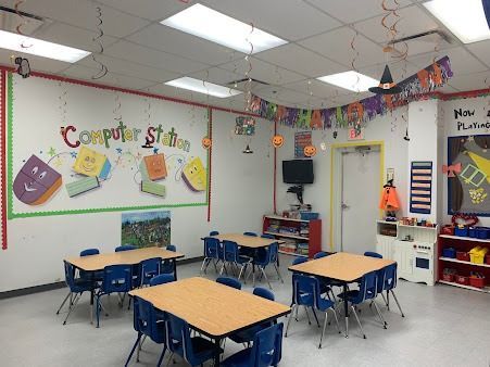 A brightly lit classroom decorated for Halloween with tables, chairs, and a computer station wall display.