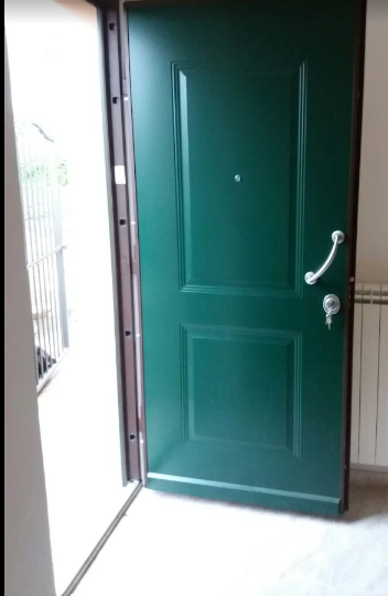 Porta d'ingresso verde aperta con maniglia argentata, socchiusa in un luminoso atrio.