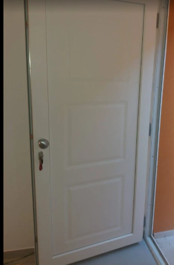 Porta interna a pannelli bianchi con maniglia e serratura argentate, mostrata in un corridoio.