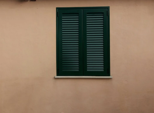 Porta chiusa con persiane in legno marrone in una parete bianca con soglia in pietra.