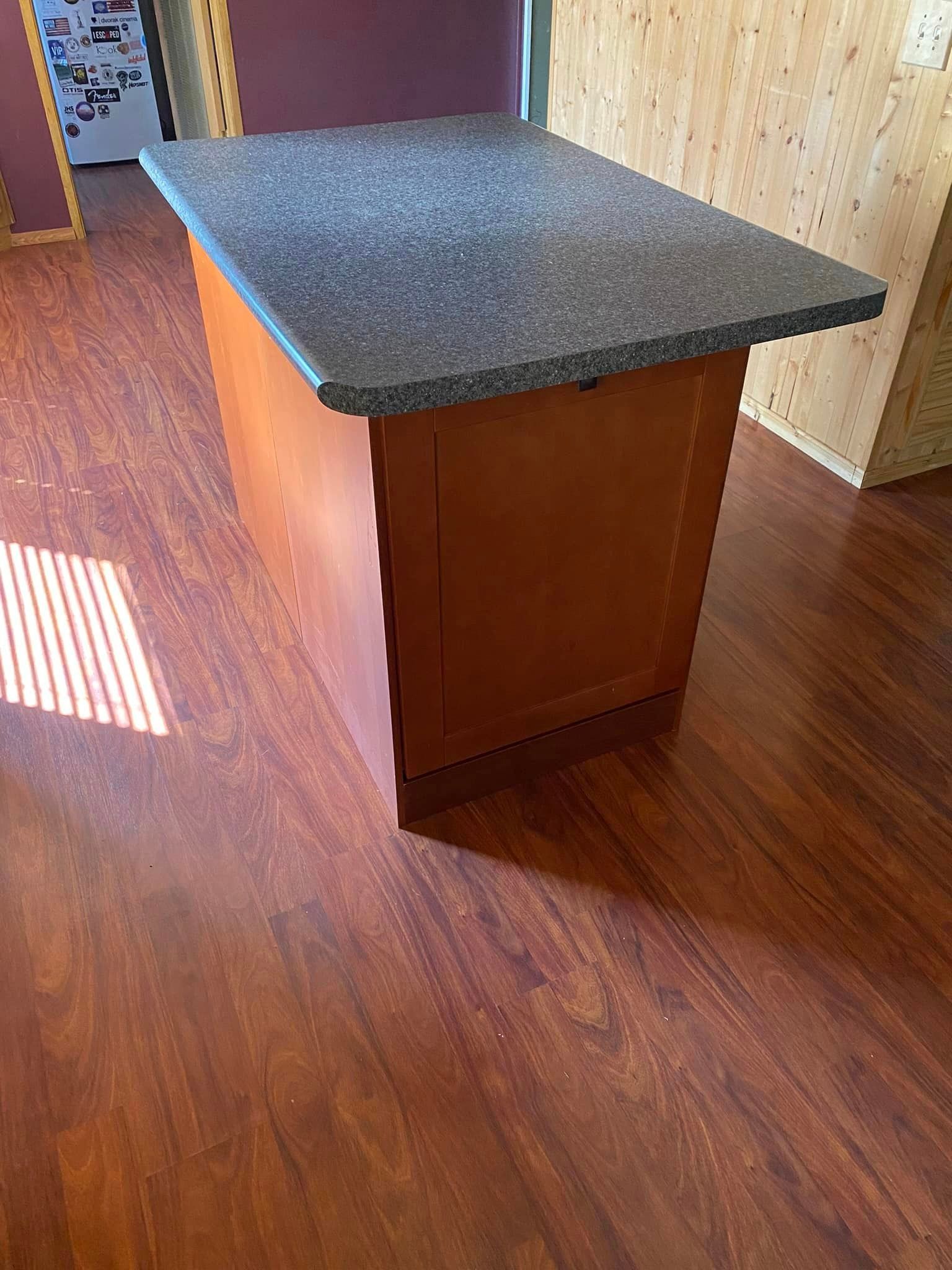 A kitchen island with a granite counter top and wooden cabinets.