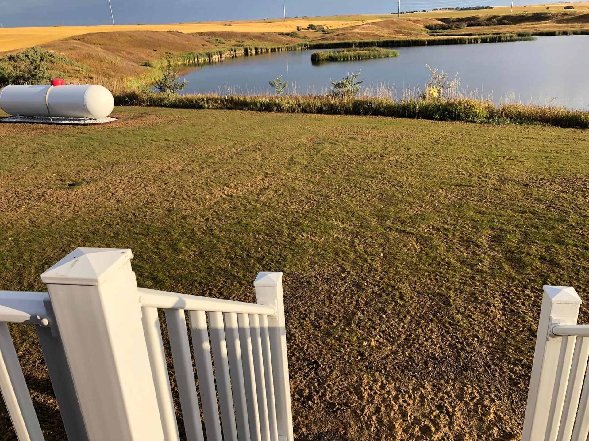 A propane tank is sitting in the grass next to a lake.