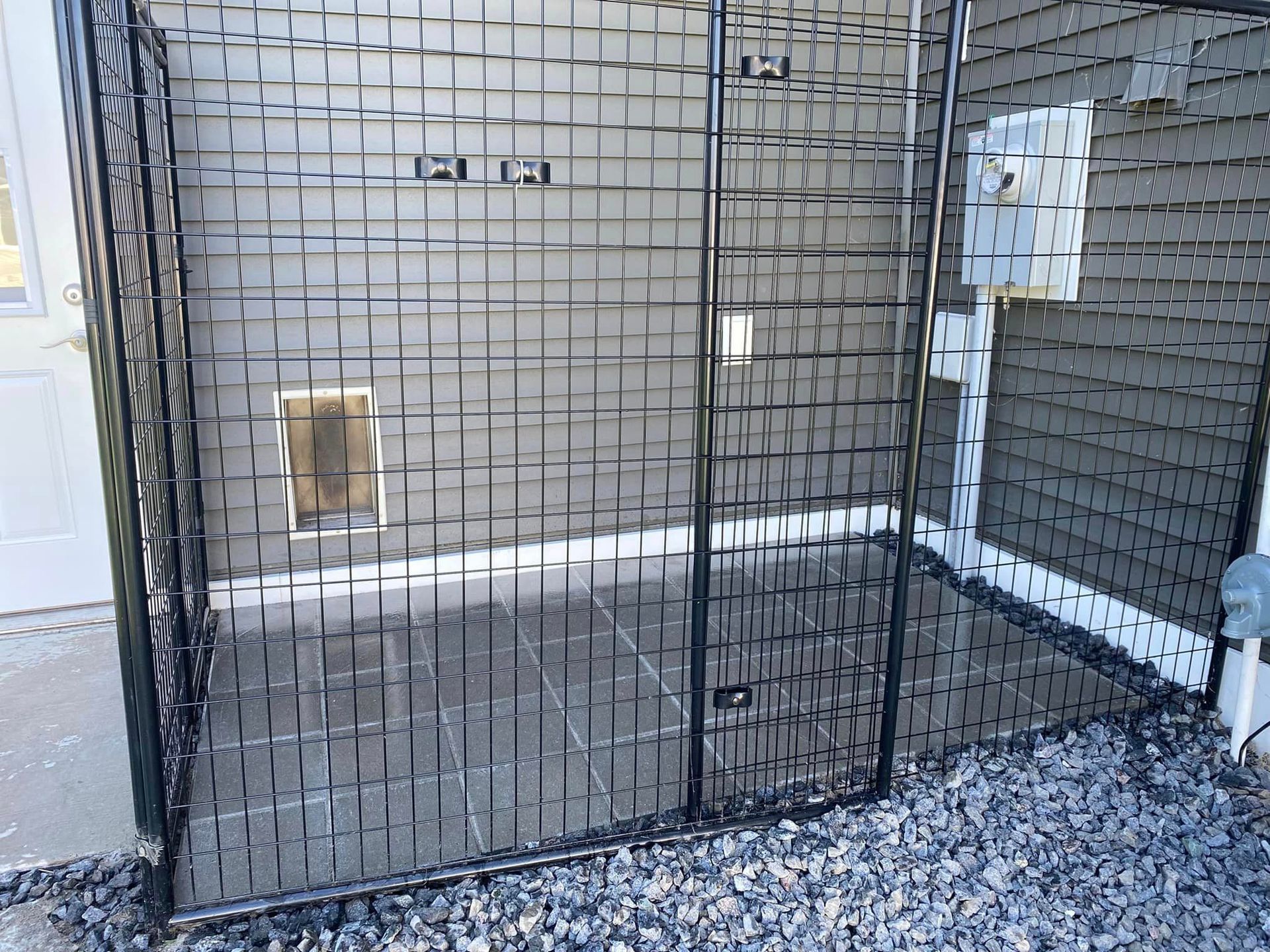 A dog kennel with a dog door in the backyard of a house.