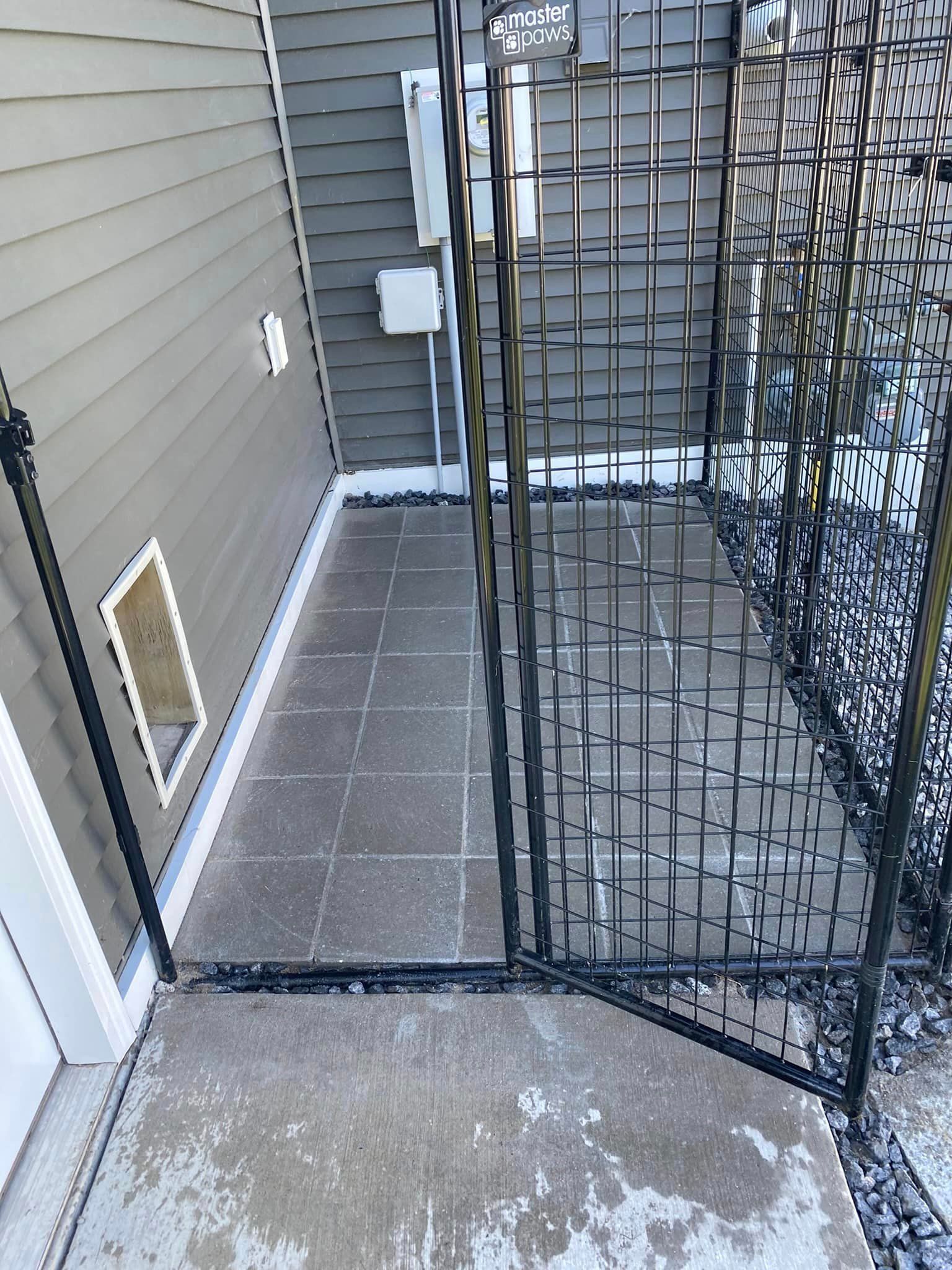 A dog door is behind a metal fence in front of a house