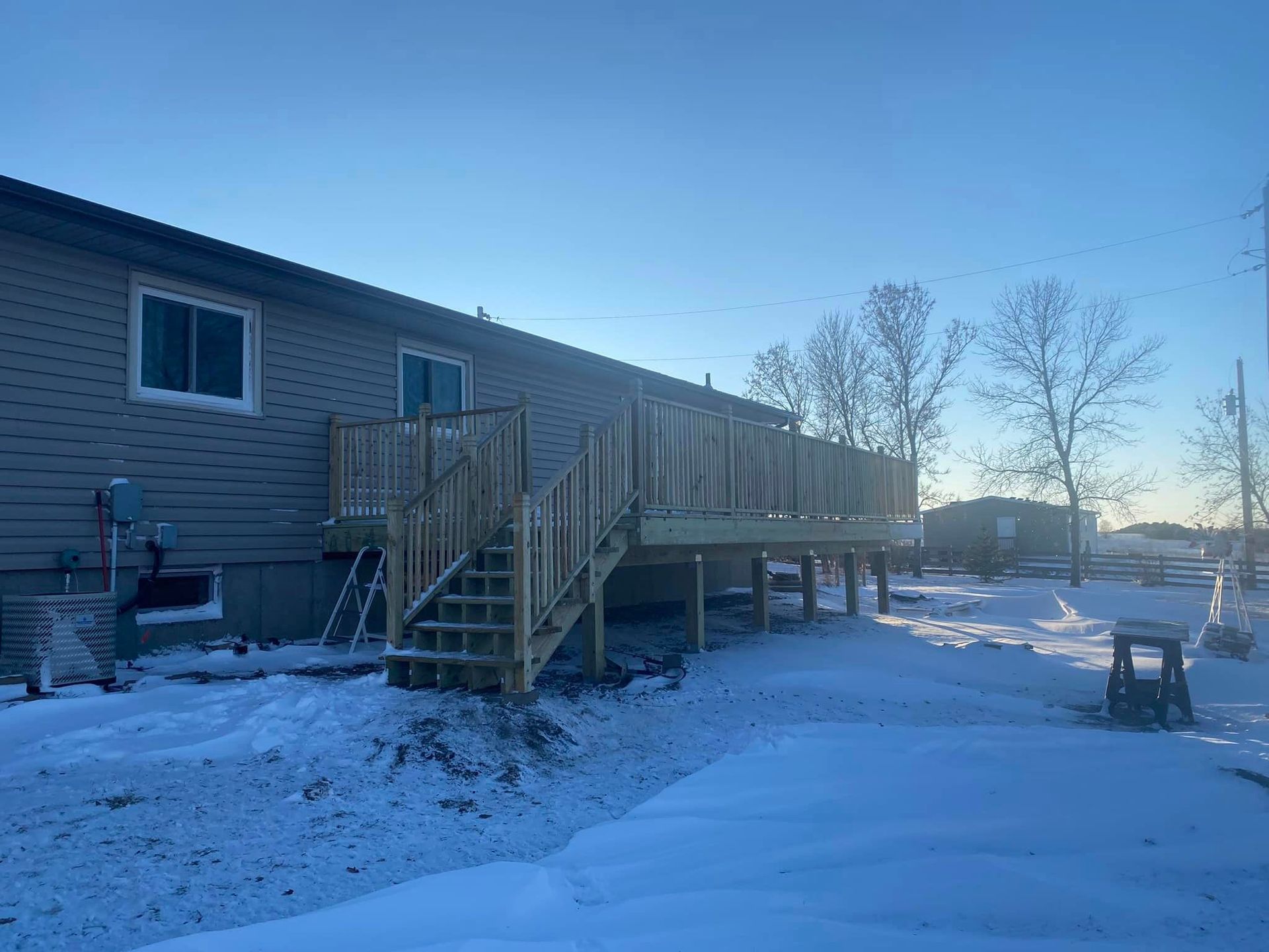 A house with a wooden deck and stairs in the snow.