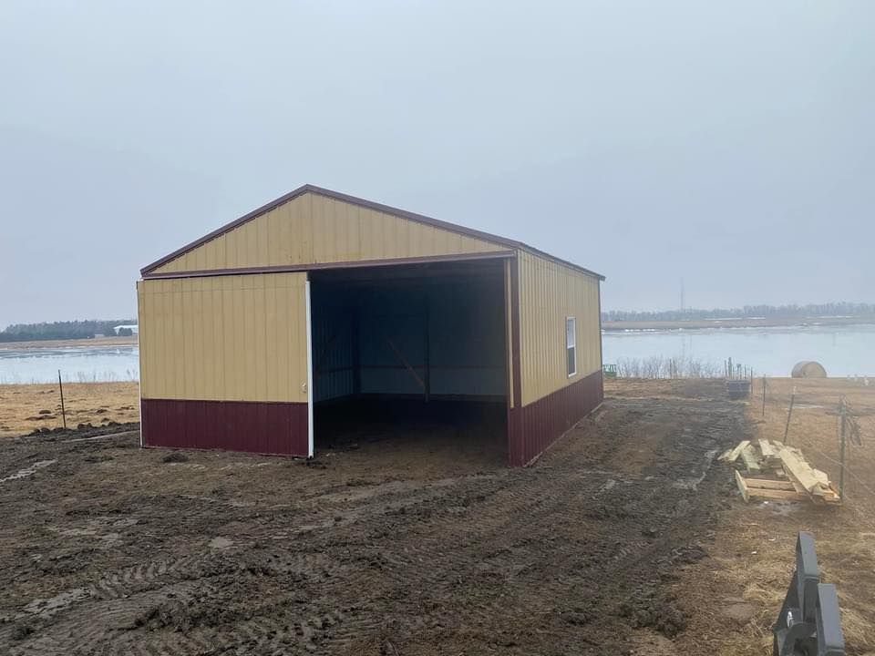 A yellow and red garage is sitting in the middle of a dirt field next to a body of water.