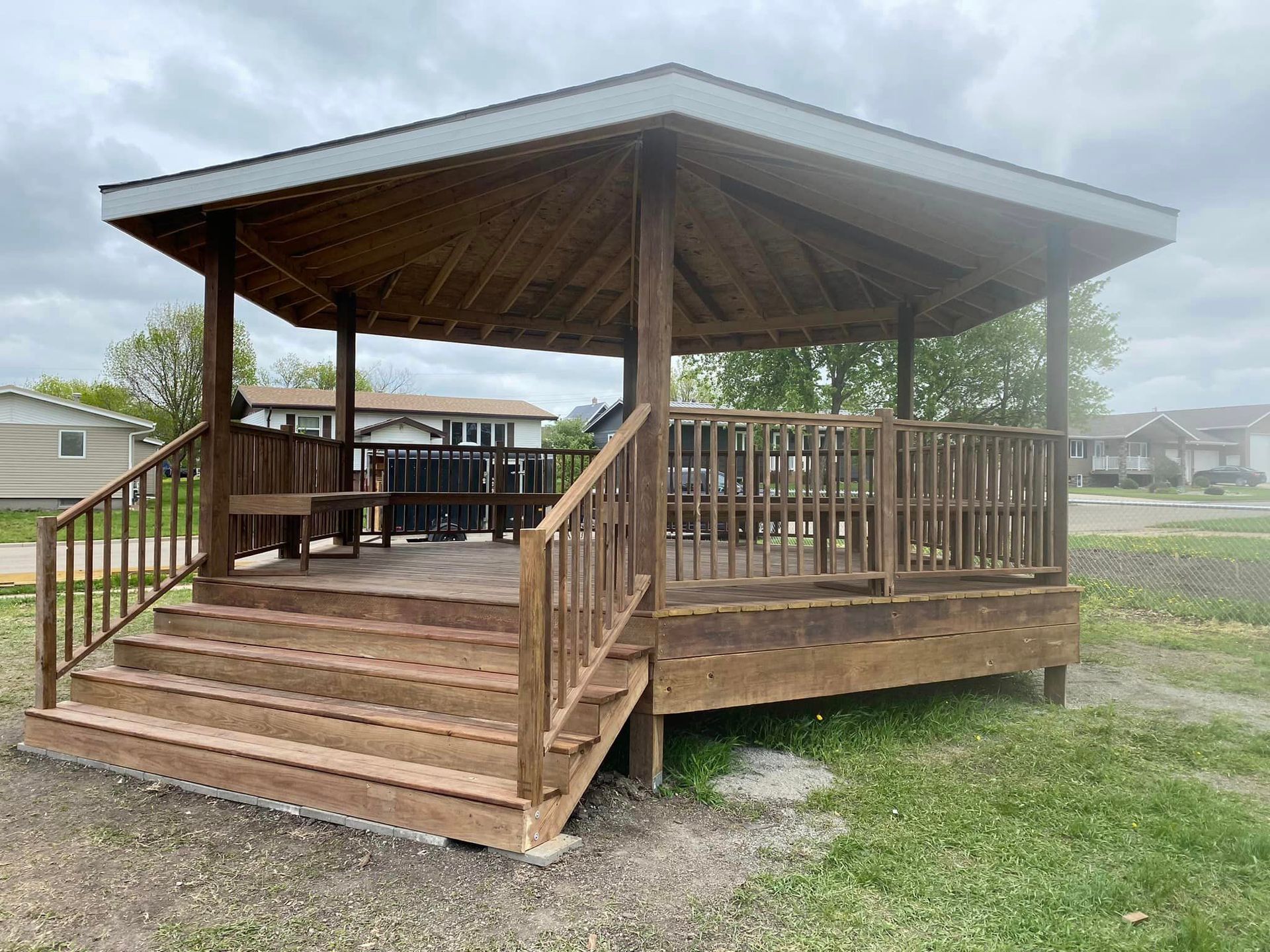 A wooden gazebo with stairs leading up to it is sitting in the middle of a grassy field.