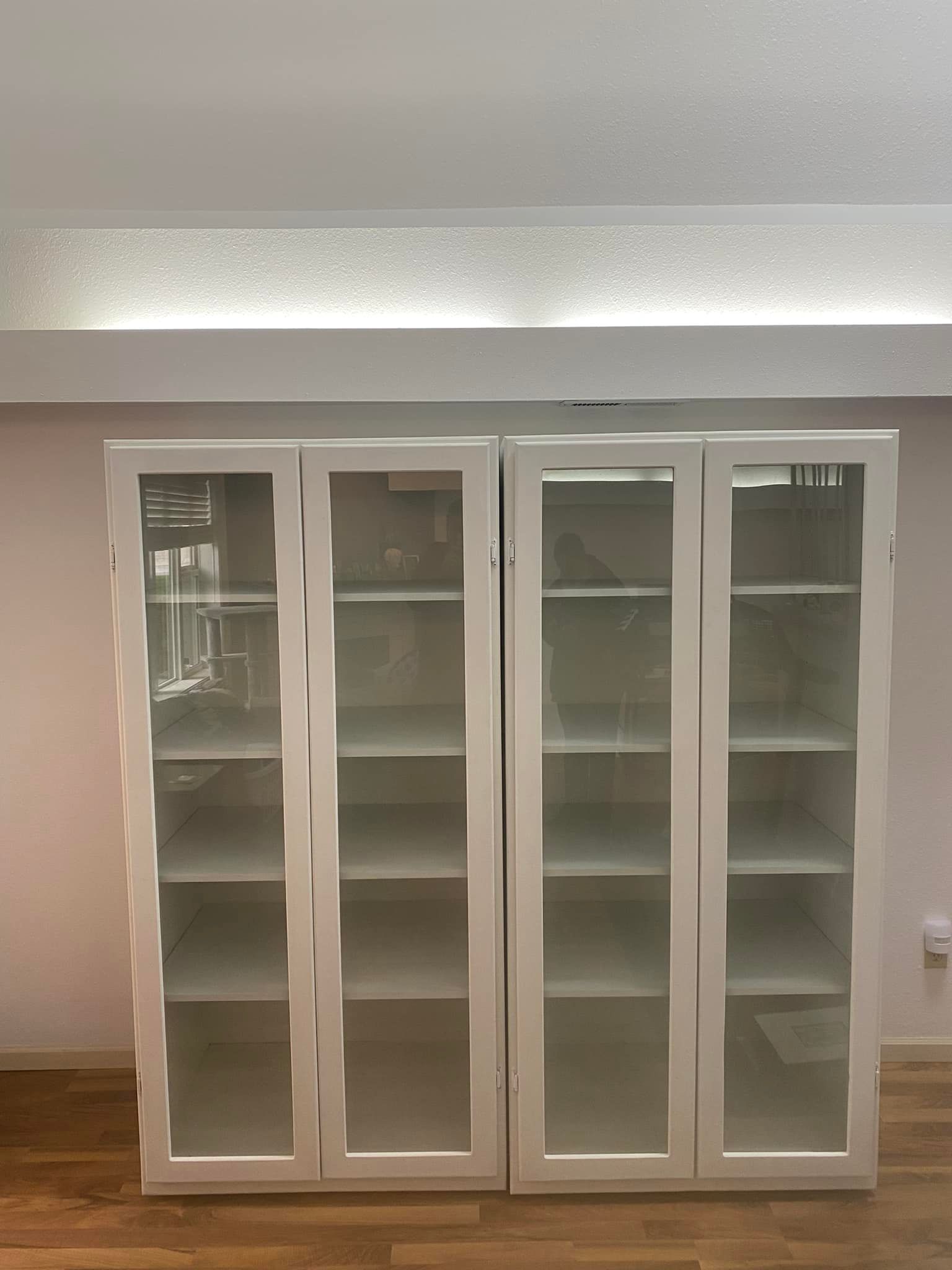 A white cabinet with glass doors and shelves in a room.