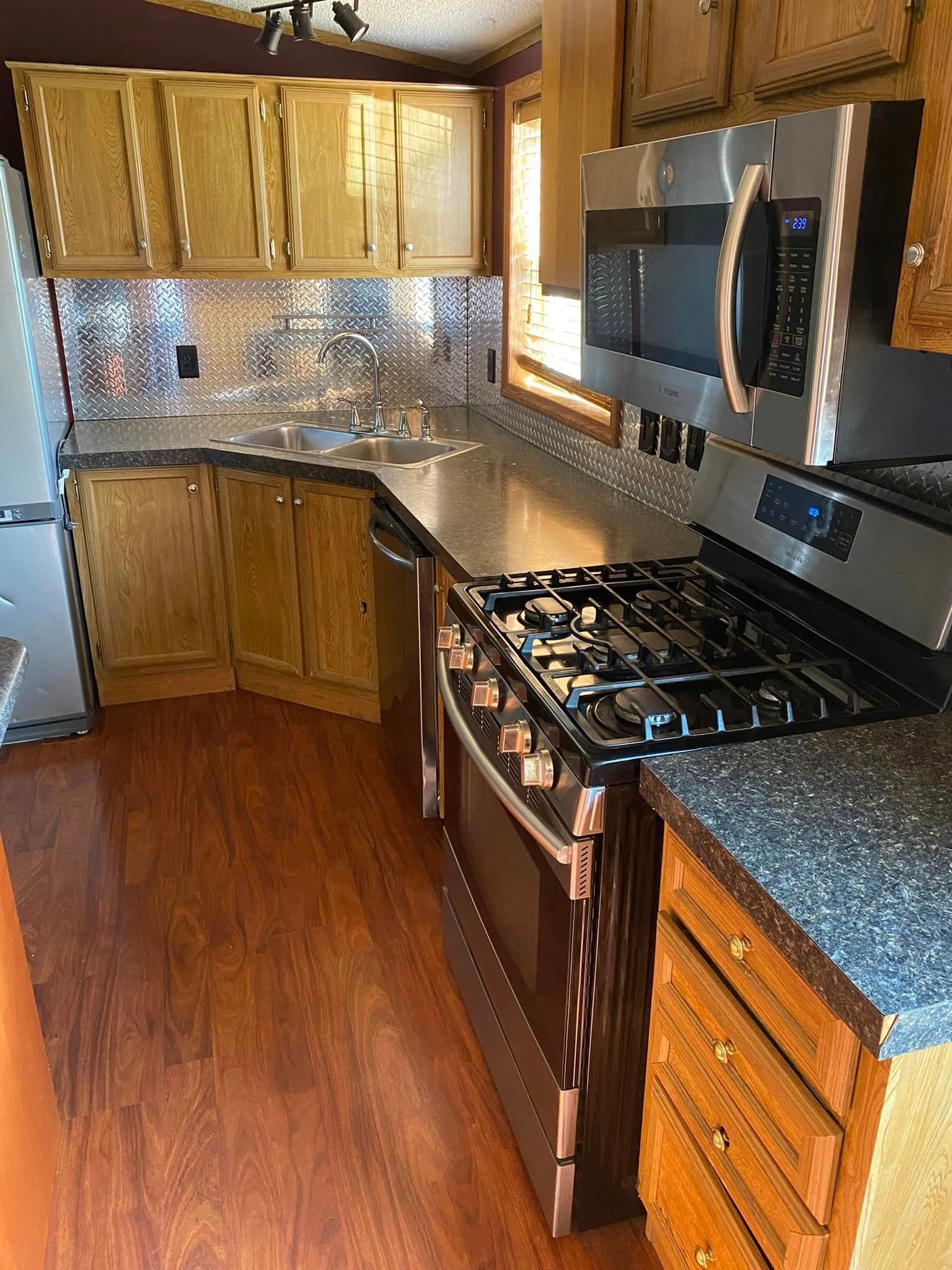 A kitchen with a stove , microwave , sink and cabinets.