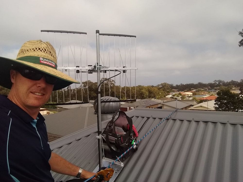 A Man Wearing A Straw Hat And Sunglasses Is Standing On A Roof — Boardman's TV Antennas in Basin View, NSW