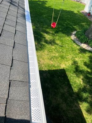 A high-angle view of a gray mesh gutter cover on a roof edge, with a red circular swing hanging in the yard below.