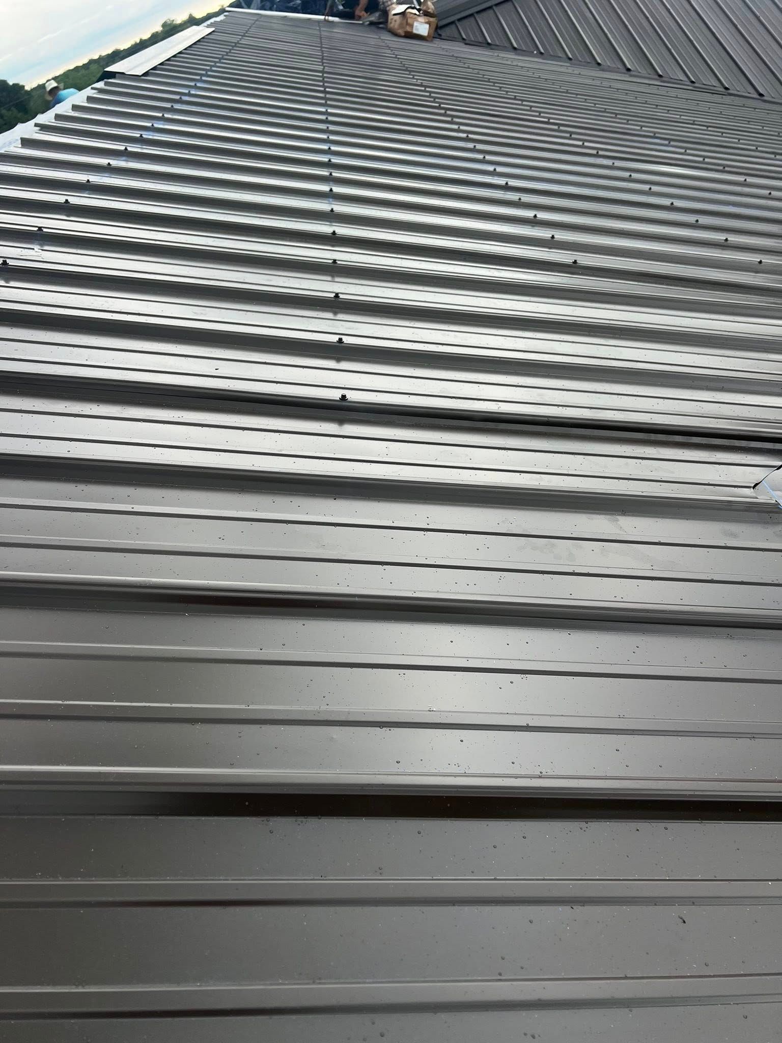 Close-up of a gray metal roof with repeating ridges and slats, viewed from below toward the peak