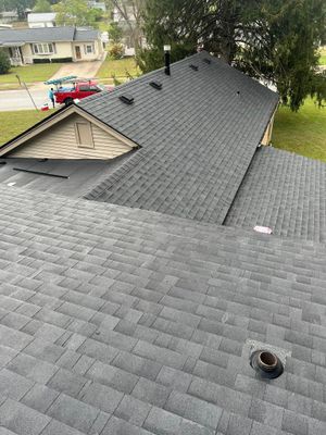 An aerial view of a dark grey shingled roof with a partial gable, plumbing vent, and a red truck parked nearby.