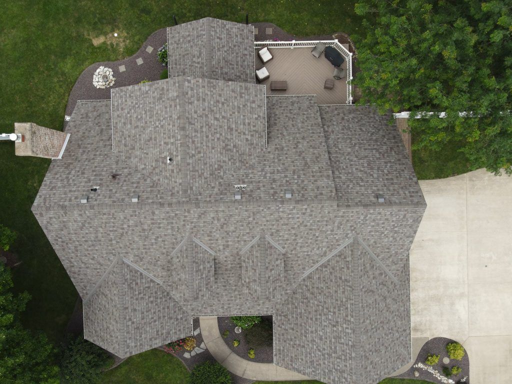 Aerial view of a gray-shingled residential roof with a rear deck and driveway.